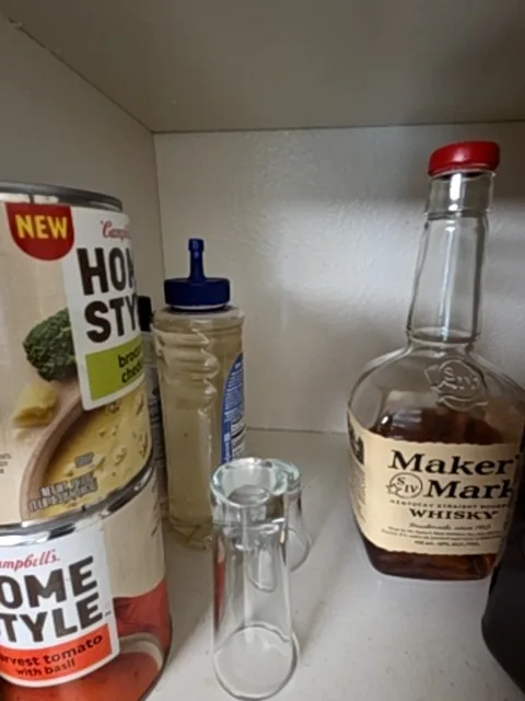 A pantry shelf with soup, whiskey, a bottle